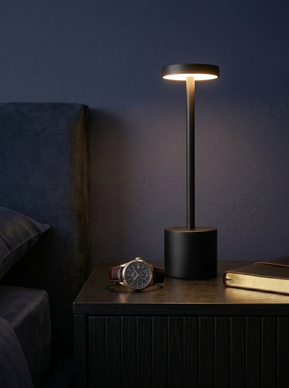 Black Egret Lamp on a bedside table beside a wristwatch in a dark bedroom