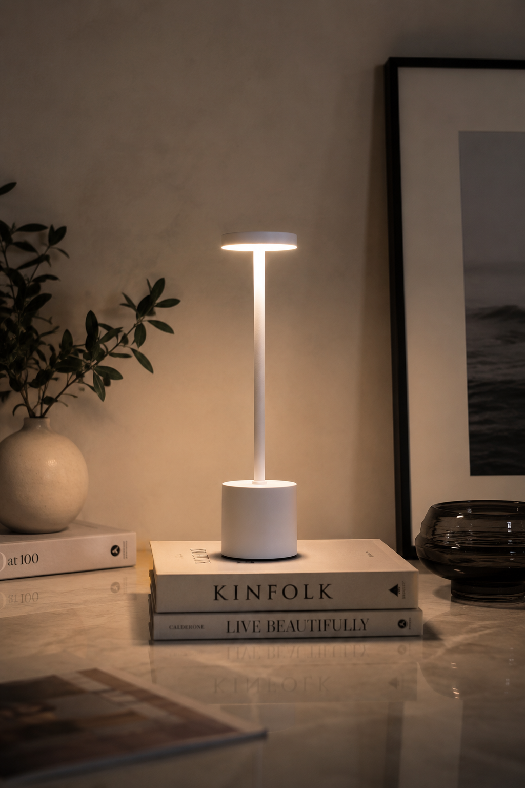 White Egret Lamp glowing on a stack of books on a marble table in a dim room