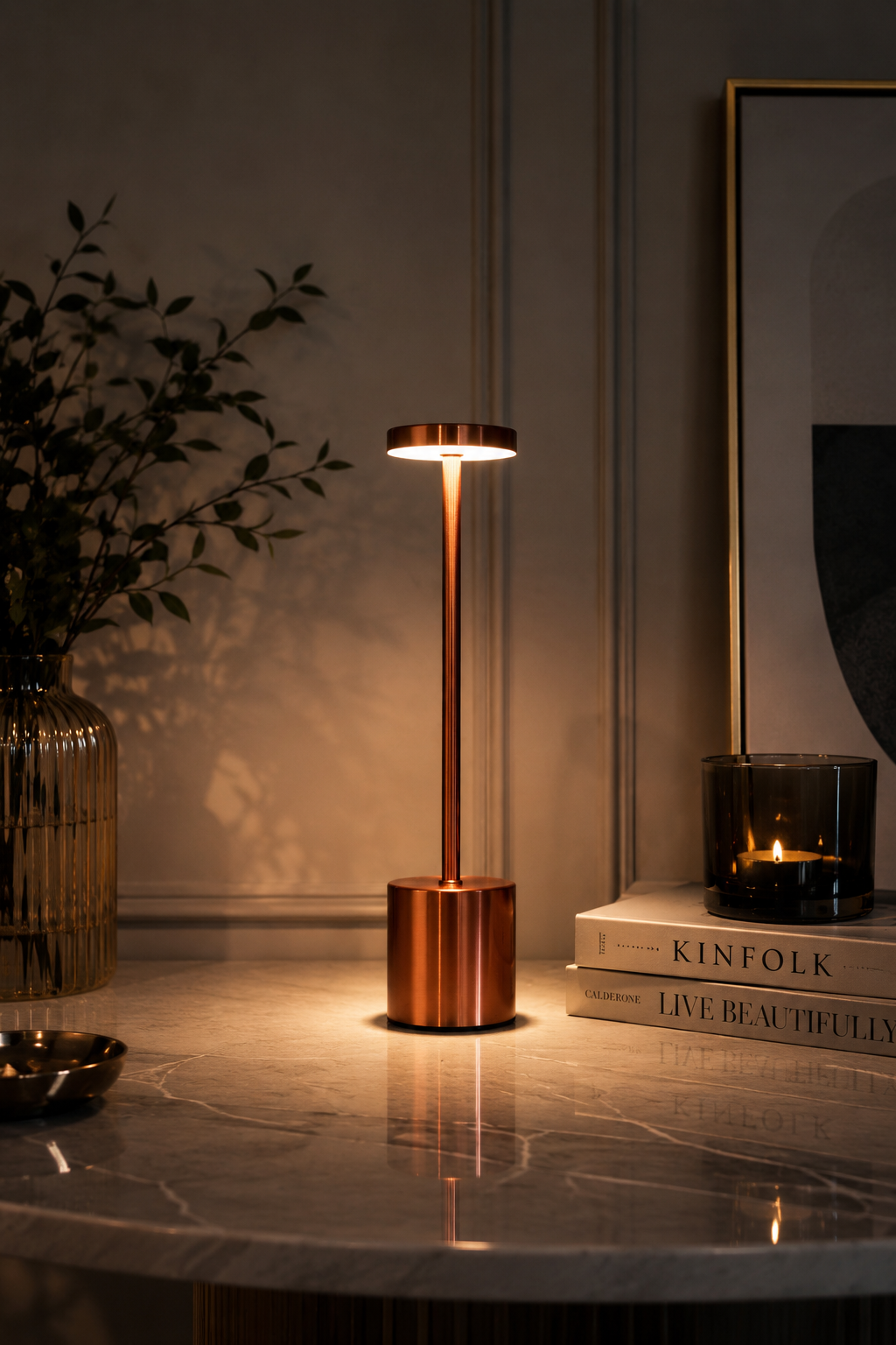 Rose Gold Egret Lamp glowing on a marble side table beside books and a candle in a dim room