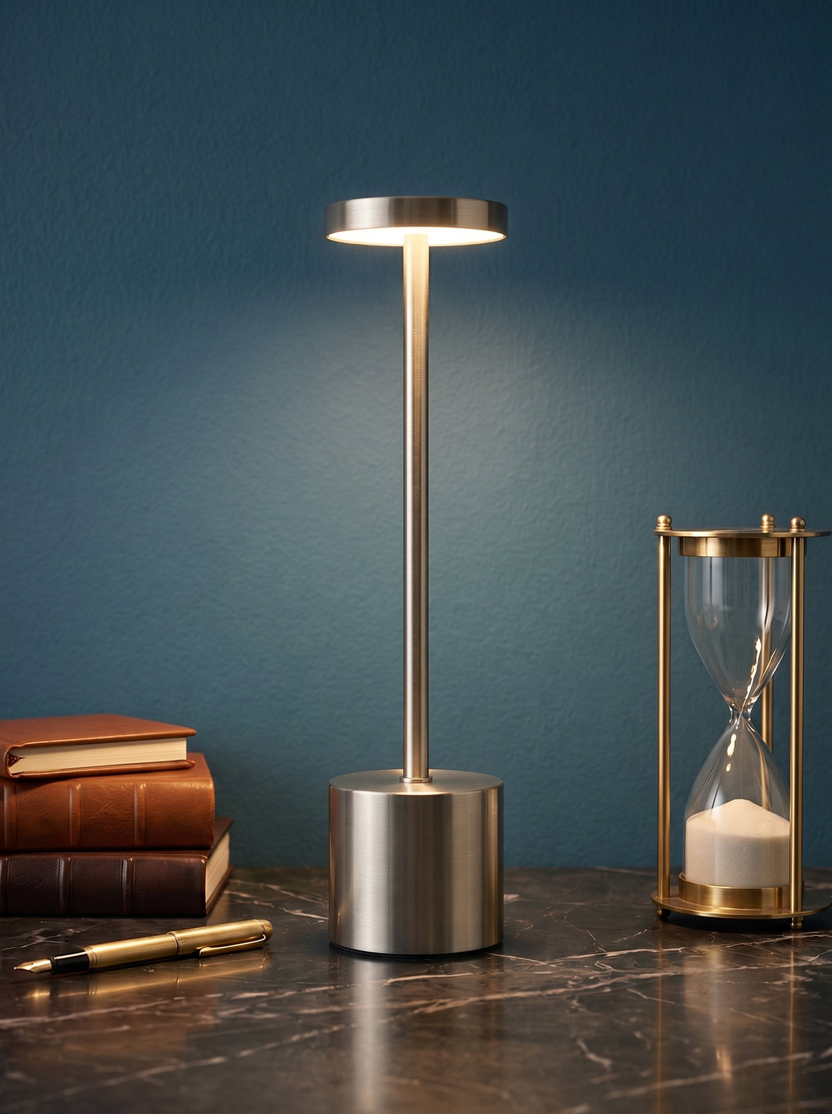 Silver Egret Lamp on a dark marble desk against a teal wall with leather books and a brass hourglass