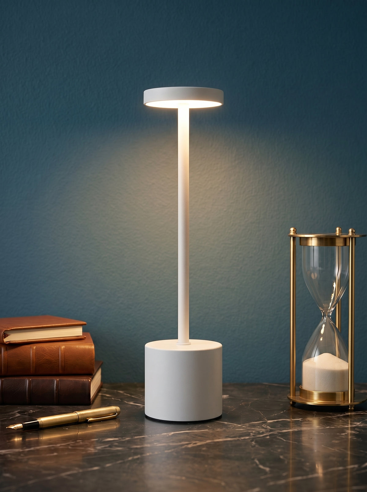 White Egret Lamp on a dark marble desk against a teal wall with leather books and a brass hourglass