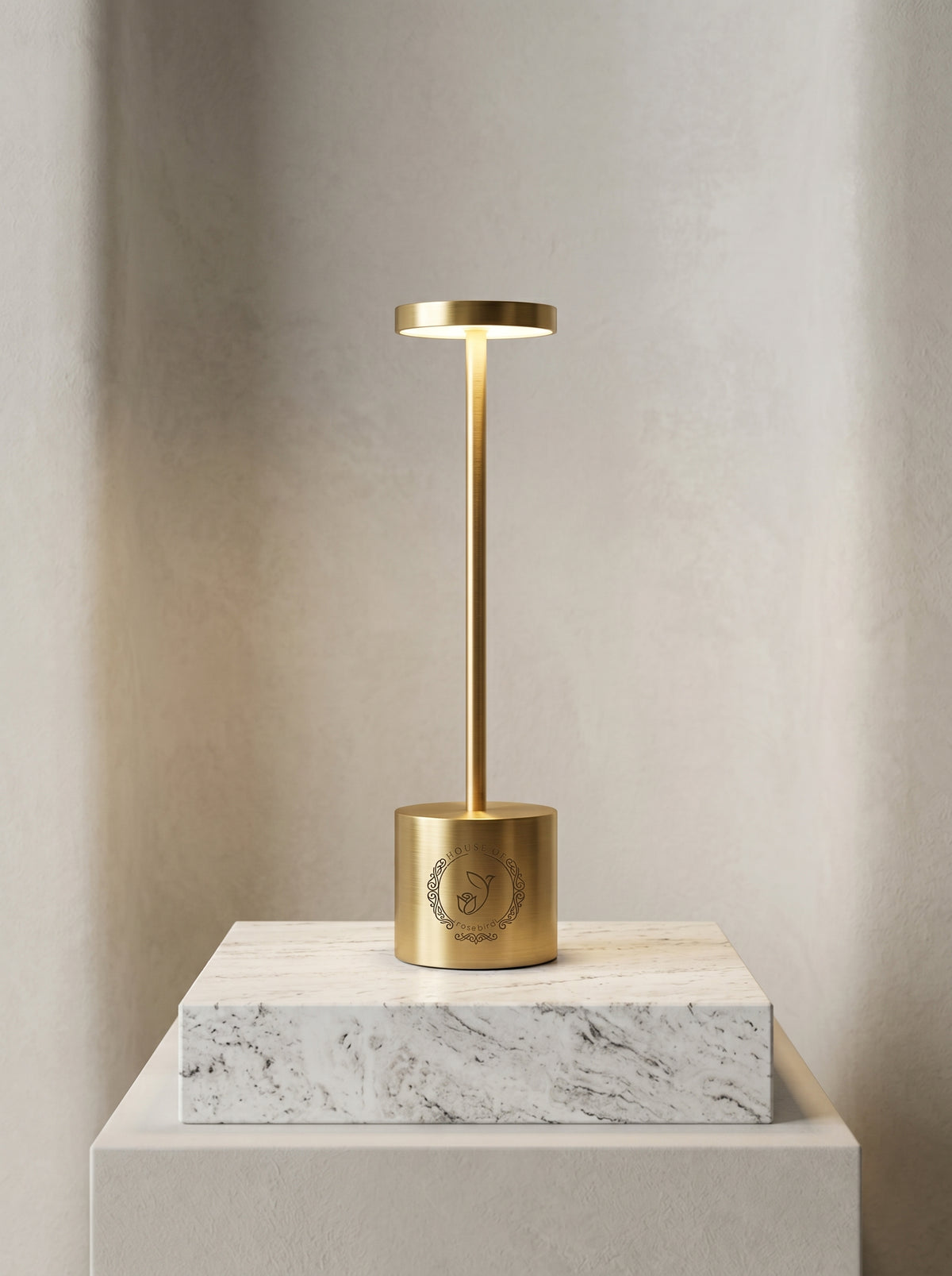 Gold Egret Lamp on a white marble block, showing the engraved logo on its base