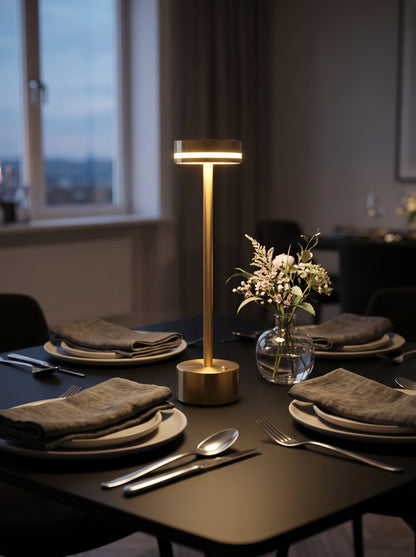 Gold Alba Lamp on a dark dining table set with plates, napkins and a small vase of flowers