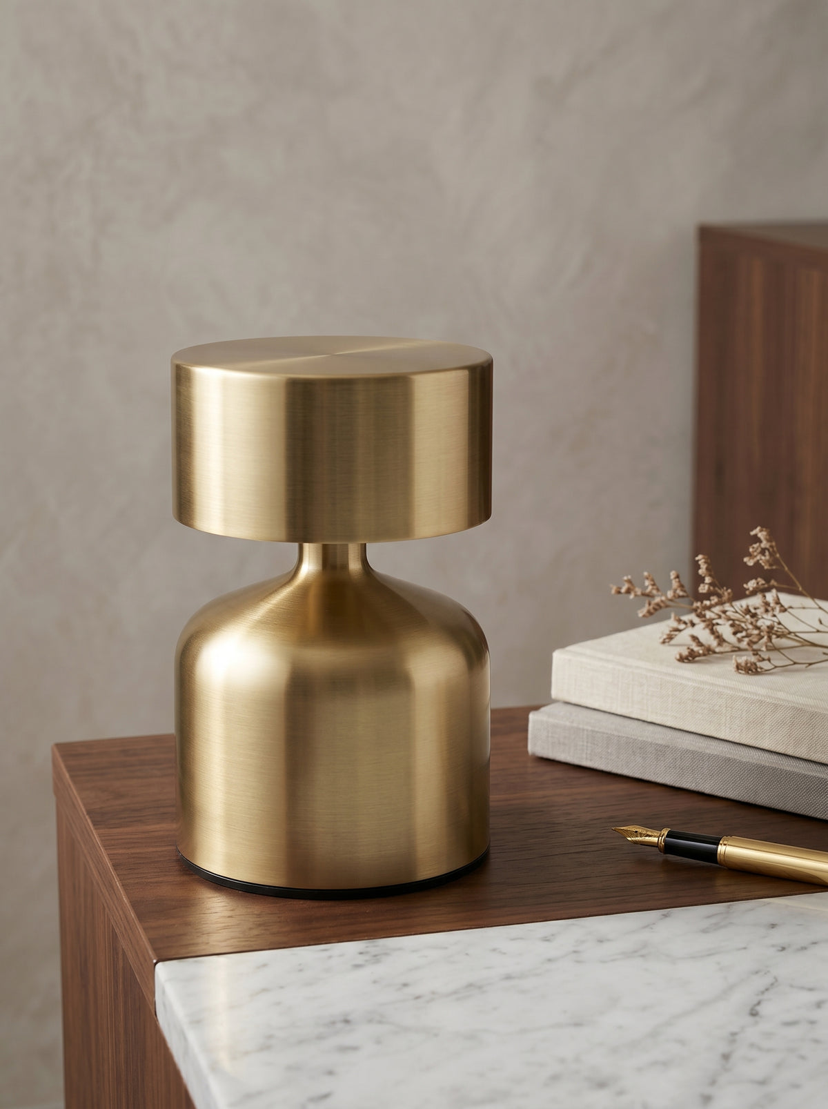Gold Pipit Lamp on a marble-topped desk with books, dried flowers and a fountain pen