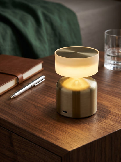 Gold Finch Lamp on a wooden desk with a leather journal, pen and a glass of water