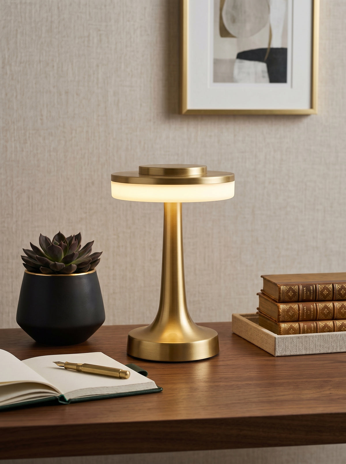Gold Kestrel Lamp on a wooden desk with a succulent, open notebook and old books