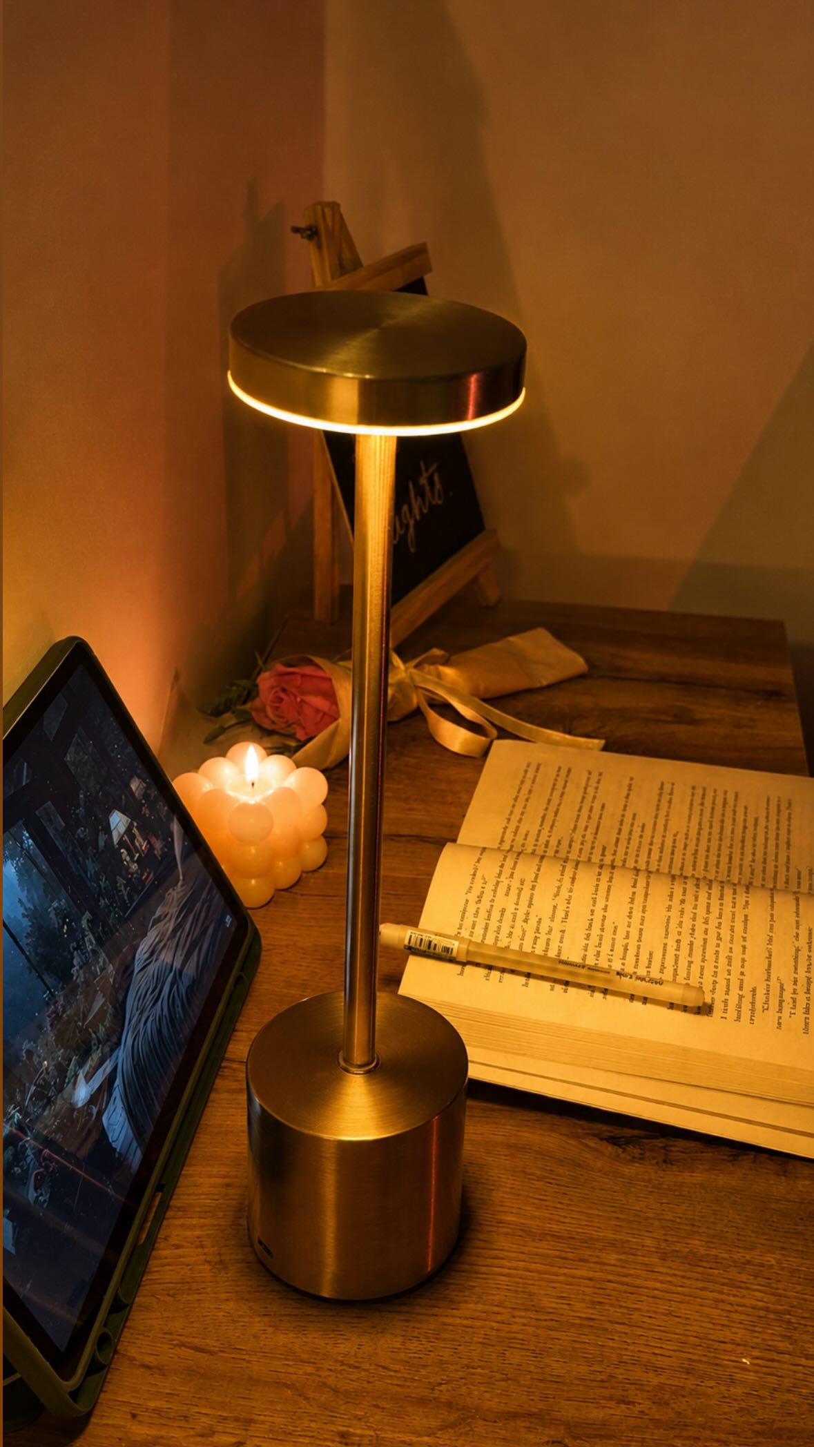Gold Egret Lamp lighting an open book beside a tablet on a bedside table at night