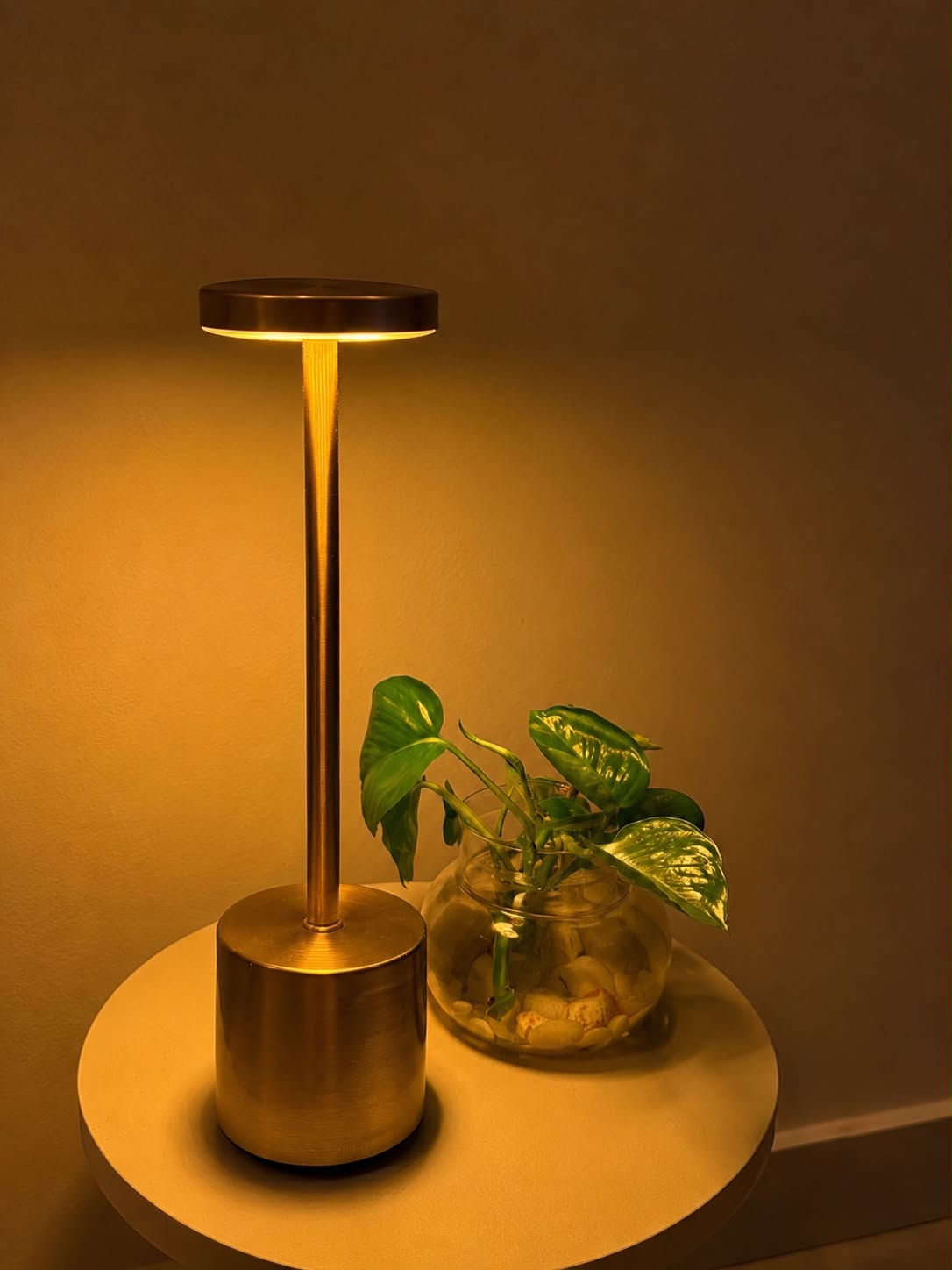 Gold Egret Lamp on a round side table beside a plant in a glass jar, in warm light