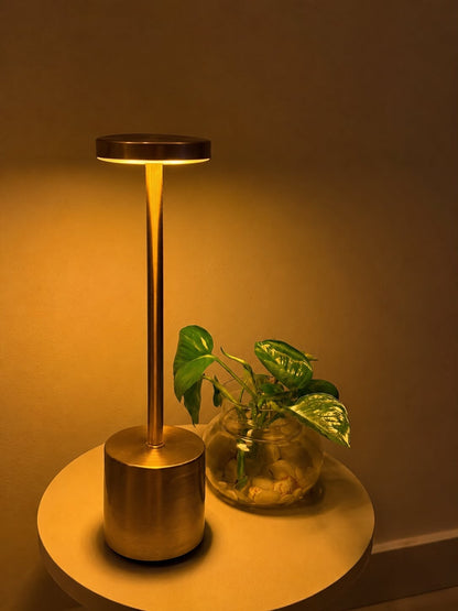 Gold Egret Lamp on a round side table beside a plant in a glass jar, in warm light