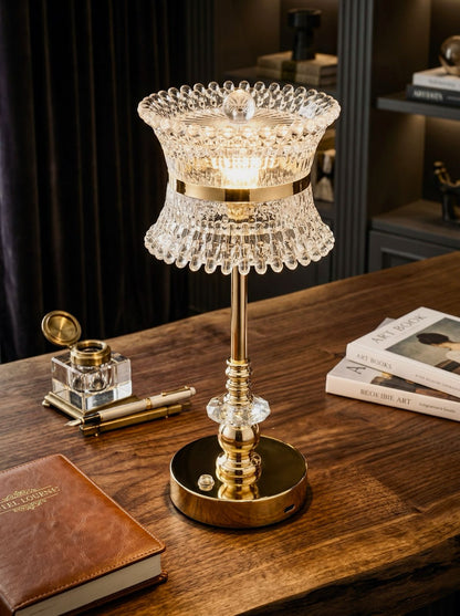 Gold Coatl Lamp, a gold lamp with a beaded glass shade and crystal stem, on a wooden desk
