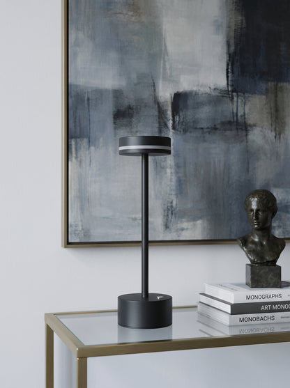 Black Alba Lamp on a glass console table with a bust sculpture and an abstract painting