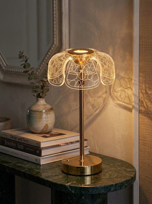 Gold Bubo Lamp, a gold lamp with a clear petal-shaped patterned shade, on a green marble console