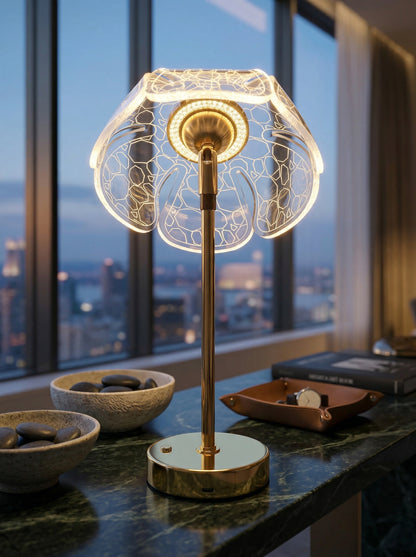 Gold Bubo Lamp glowing on a marble table in front of a city view at dusk