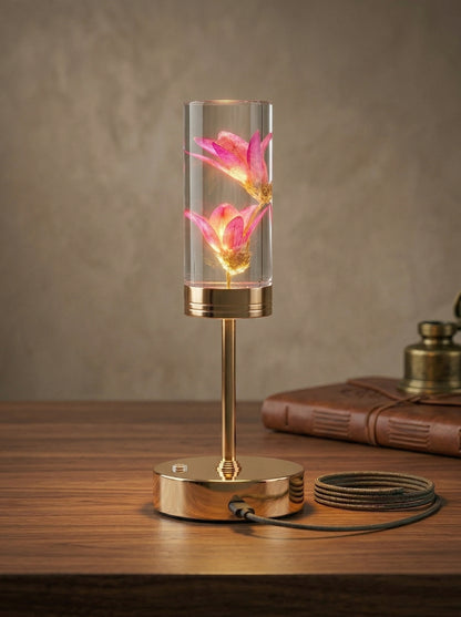 Gold and Pink Phoenix Lamp on a wooden table beside a leather book and brass accents