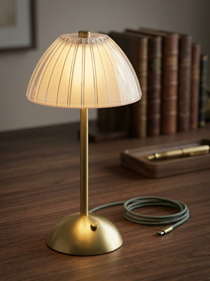 Gold Serin Lamp, a gold lamp with a ribbed frosted dome shade, on a wooden desk