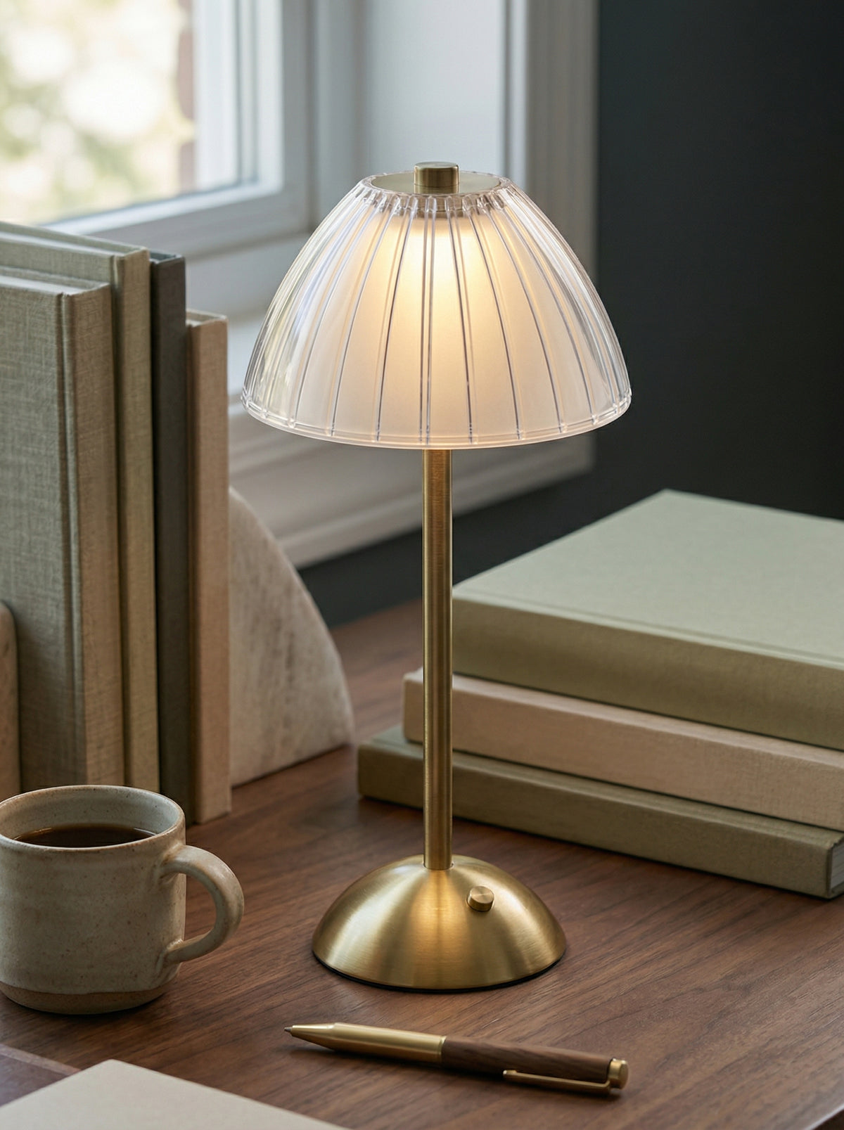 Gold Serin Lamp on a desk by a window with books and a mug of coffee