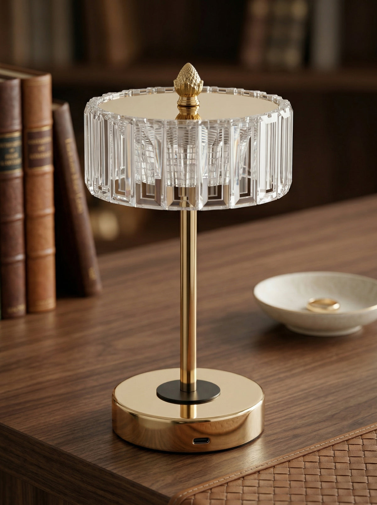 Gold Starling Lamp on a wooden desk in front of old leather-bound books