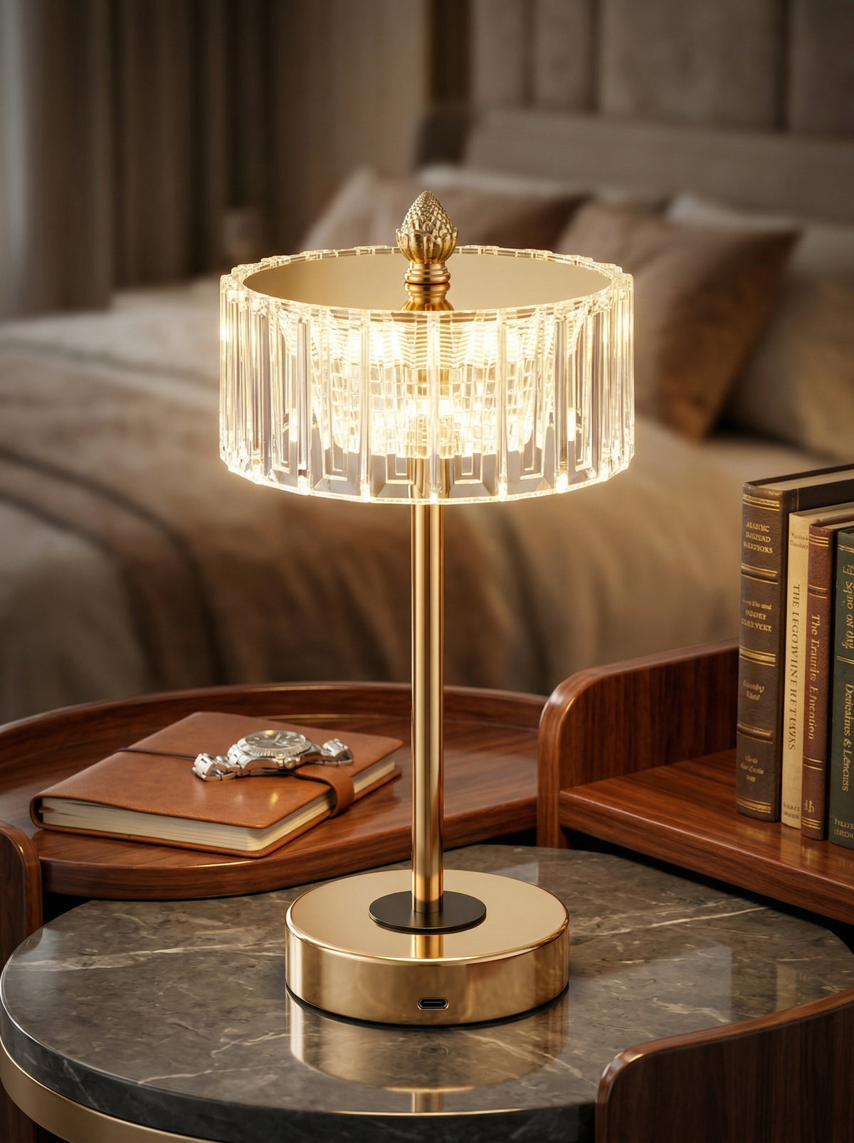Gold Starling Lamp glowing on a marble bedside table beside books and a leather notebook