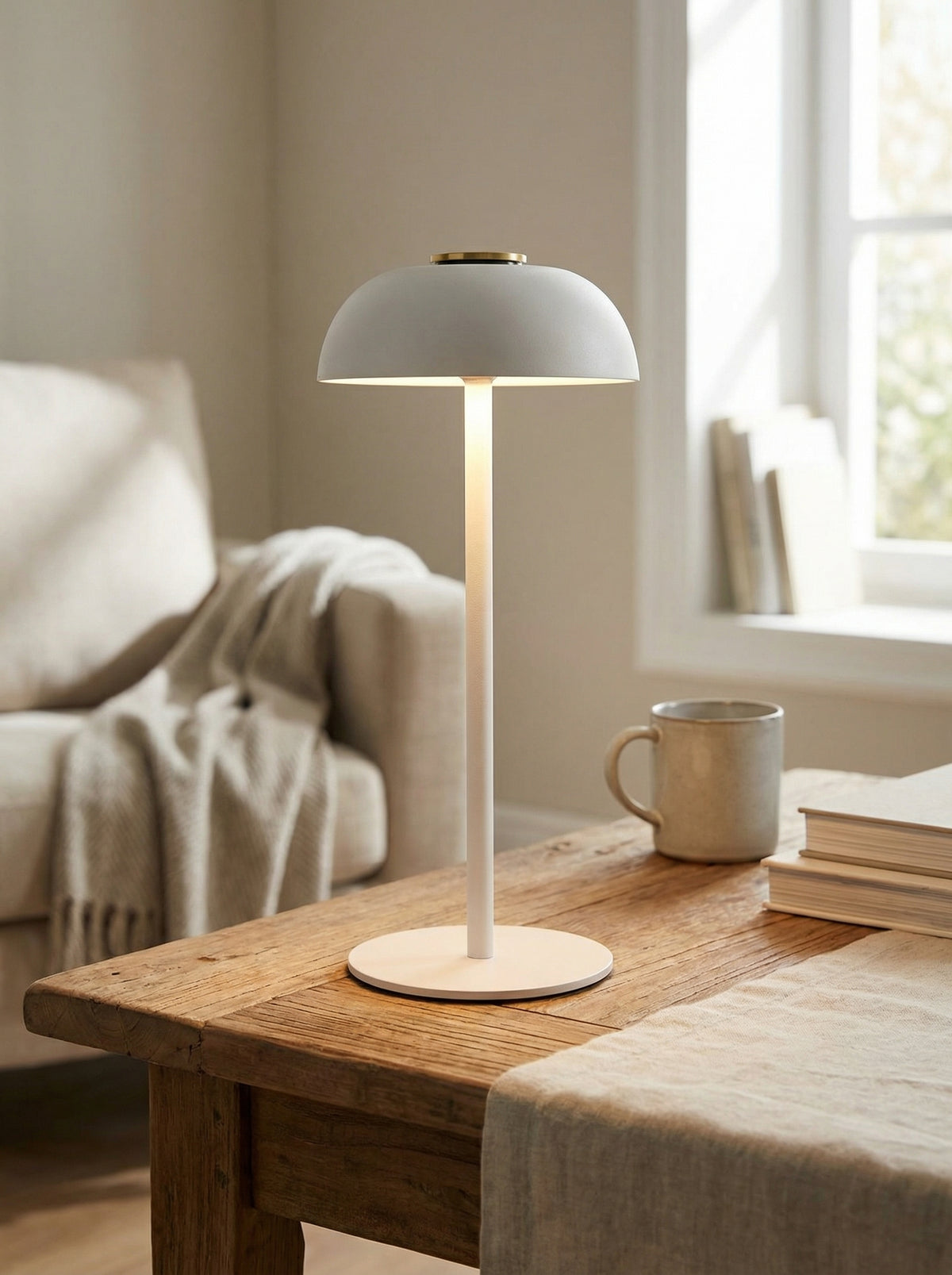White Swan Lamp with a matte dome shade and slim stem on a wooden table beside a sofa and mug